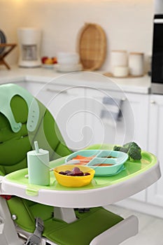 High chair with food in baby tableware on tray indoors