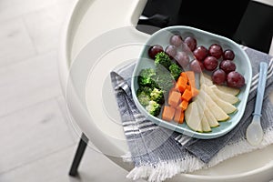 High chair with food in baby tableware on tray indoors, closeup. Above view