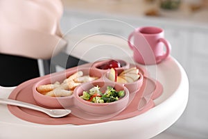 High chair with food in baby tableware on white tray indoors, closeup