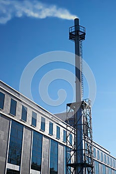 High chimney made of stainless steel of an industrial gas boiler with smoke coming out of it steam. Building with autonomous