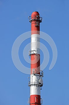 High chimney at the plant in red-white color with equipment for broadcasting radio. Installing a cellular antenna. Combining the