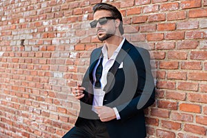high class businessman with sunglasses opening suit and looking away