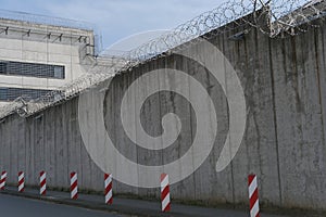 high concrete fence, barbed wire fence on top, pre-trial detention cell, building for execution of punishments for criminals,