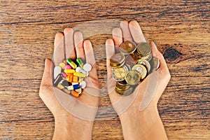 High cost of medical pills concept with piles of coins and pharmaceutical drugs in woman hands with wooden background