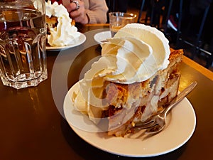 High Dutch apple pie with plenty of whipped cream on a brown wooden table with a cup of hot tea in winter