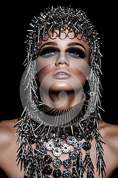 High fashion beauty model with metallic headwear and dark makeup and blue eyes on black background