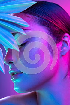 High fashion model in colorful bright neon lights posing at studio. Portrait of beautiful girl with trendy glowing make