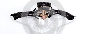 High fashion model. Female model is wearing black biker hat and long leather gloves and is posing on white background. Vogue