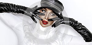 High fashion model. Female model is wearing black biker hat and long leather gloves and is posing on white background. Vogue