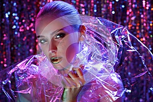 High Fashion model girl in colorful bright neon lights posing in studio through transparent film. Portrait of beautiful