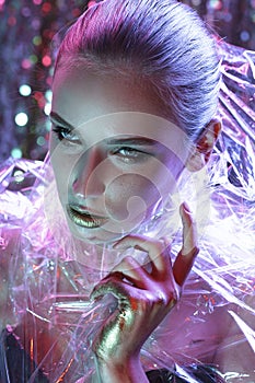 High Fashion model girl in colorful bright neon lights posing in studio through transparent film. Portrait of beautiful