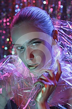 High Fashion model girl in colorful bright neon lights posing in studio through transparent film. Portrait of beautiful