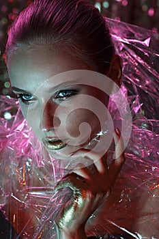 High Fashion model girl in colorful bright neon lights posing in studio through transparent film. Portrait of beautiful