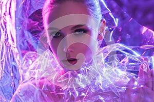 High Fashion model girl in colorful bright neon lights posing in studio through transparent film. Portrait of beautiful