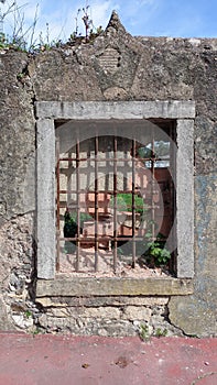 High fence with window and grille. Antique window covered with red brick