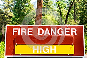 High fire danger sign informs the public that wildfires are likely. Green forest background