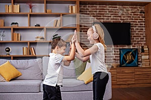Children jump and dance at home while listening to music on headphones. Having fun. Family concept
