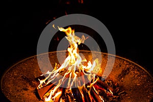 High flames from a burning wood fire on a metal grate at night.