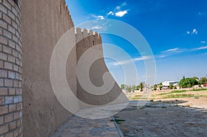 High fortress walls with crenellations lead to a corner tower against a clear sky, near modern buildings photo