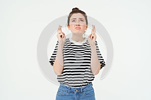 High hopes. Young woman cross fingers, makes wish, anticipates something, stands over white background