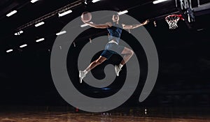 Young African sportsman, basketball player jumping high isolated on dark background. Concept of sport, game, competition