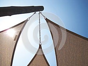 HIGH KEY IMAGE OF SUN BEHIND RIGGED CANVAS COVER AGAINST THE BLUE SKY