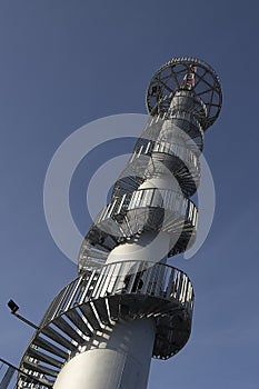 High lookout tower with spiral metal stairs against a beautiful blue sky