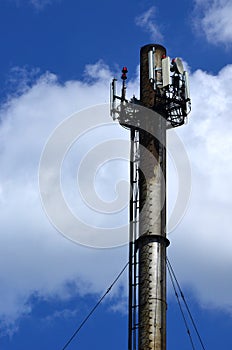 High metal chimney of industrial plant with ladder in the form of metal braces against the background of a cloudy blue sk