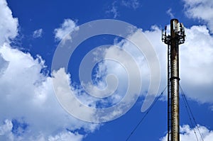 High metal chimney of industrial plant with ladder in the form of metal braces against the background of a cloudy blue sk