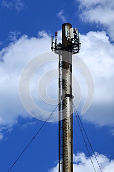 High metal chimney of industrial plant with ladder in the form of metal braces against the background of a cloudy blue sk