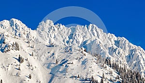 High mountain with summit cross under deep snow in winter. Rauhhorn, Allgau, Bavaria in Germany.