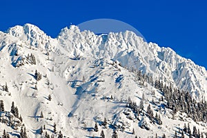 High mountain with summit cross under deep snow in winter. Rauhhorn, Allgau, Bavaria in Germany.