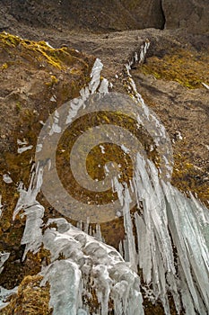 High mountain wall to the top with moss and fang-like stalagtites next to the Kvernufoss waterfall in Iceland photo