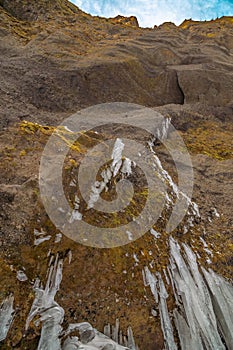 High mountain wall to the top with moss and fang-like stalagtites next to the Kvernufoss waterfall in Iceland photo