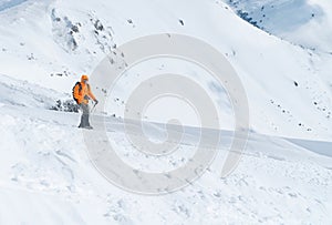 Svetlooranžová softshellová bunda vo vysokohorskom oblečení s trekingovými palicami na výstup na zasnežený vrchol hory. Aktívni ľudia