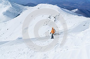 High mountaineer dressed bright orange softshell jacket using a trekking poles ascending the snowy mountain summit. Active people