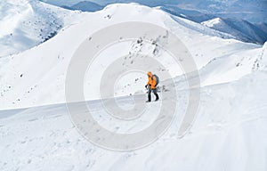 High mountaineer dressed bright orange softshell jacket using a trekking poles ascending the snowy mountain summit. Active people