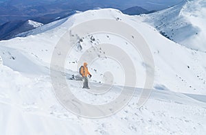 High mountaineer dressed bright orange softshell jacket using a trekking poles ascending the snowy mountain summit. Active people