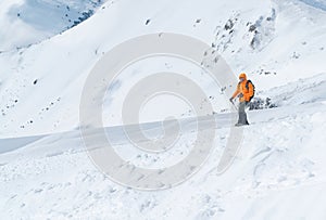 High mountaineer dressed bright orange softshell jacket using a trekking poles ascending the snowy mountain summit. Active people