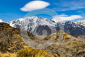 High mountains with snow on top in the winter, beautiful skies and clouds. The grass is yellow in Mount Cook Rd