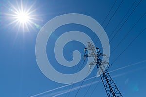 High power electrical lines electricity pylon in blue sky with sun