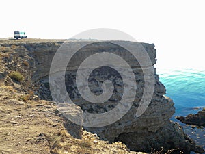 A high precipitous coastal rocky cliff with a tourist bus on top.
