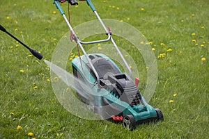 High-pressure washer washes lawn mower with jet of water on green grass