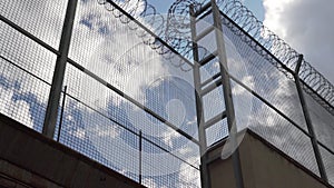 High prison fence with barbed wire against the blue sky. camera rises slowly up