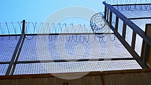 High prison fence with barbed wire, bottom view. Prison fence against clear sky.