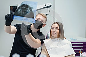 High-qualified dentist shows the young female patient an X-ray of the teeth in the dental chair at modern clinic.