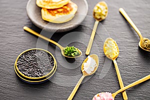 High quality real black sturgeon caviar in a golden tin can aside blinis in a plate and golden spoons with pickles and herbs.