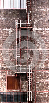 High red and white iron staircase with intermediate platforms of lattice iron on a facade of bricks, abstract