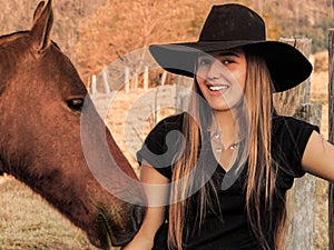 High resolution image of a pretty charming cowgirl wearing black cowboy hat next to her horse