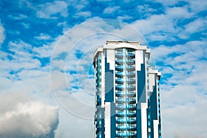 High-rise building with a glass facade against a bright blue sky with figured clouds